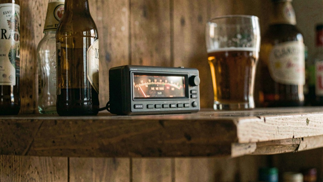 A small radio receiver on a wooden back bar shelf between two bottles, its tuning needle glowing, a pint glass beside it, warm evening light
